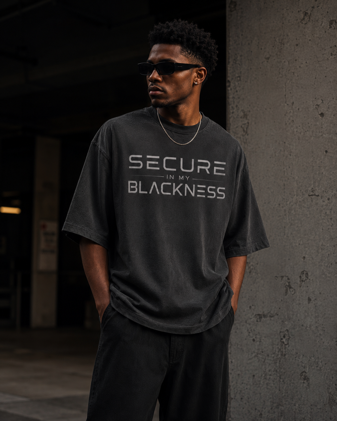 Person wearing a dark gray t-shirt with 'Secure in my Blackness' text, standing against a dark background.