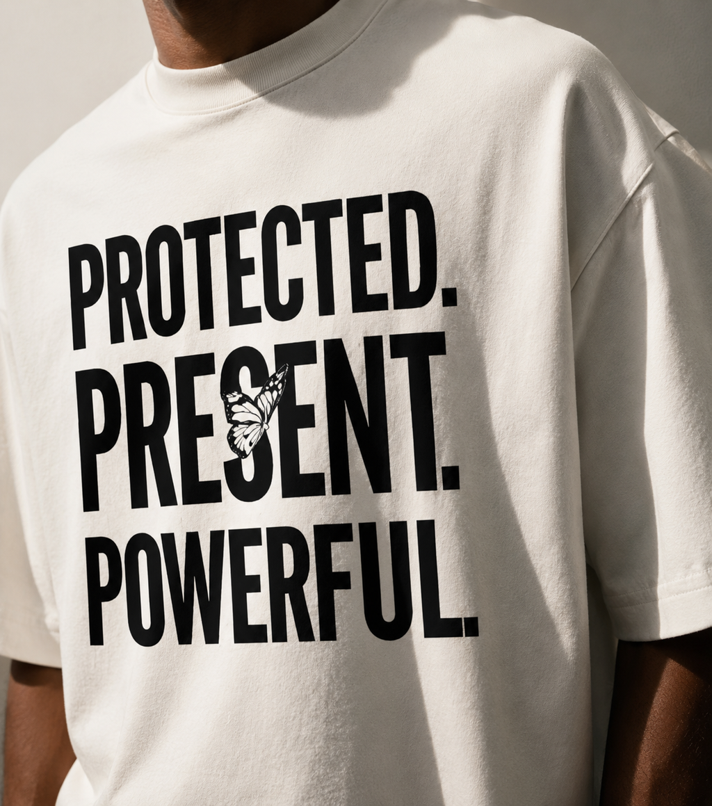 White t-shirt with motivational text 'PROTECTED. PRESENT. POWERFUL.' on a neutral background