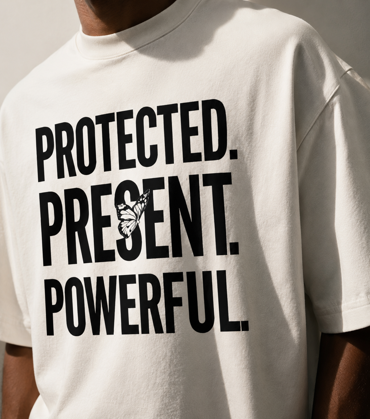 White t-shirt with motivational text 'PROTECTED. PRESENT. POWERFUL.' on a neutral background
